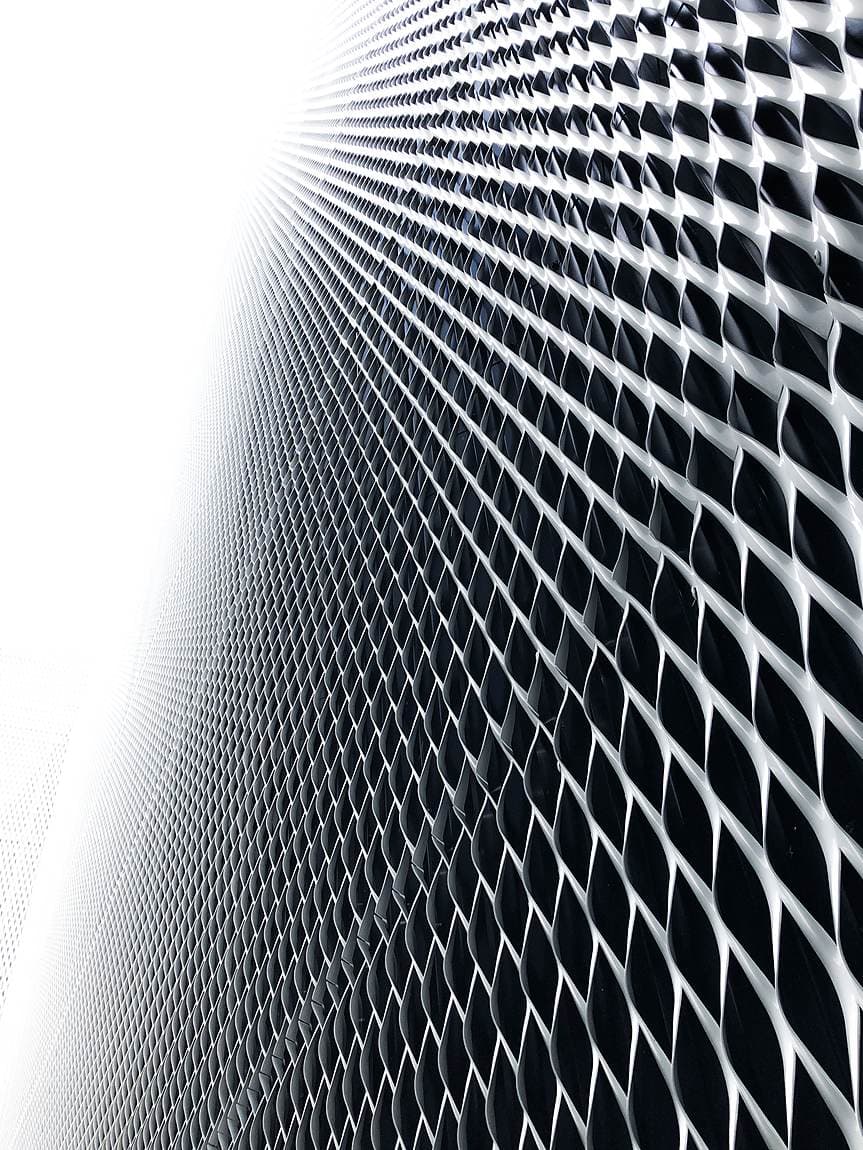 Close-up of an expanded metal mesh facade in a repeating diamond pattern, fading to white